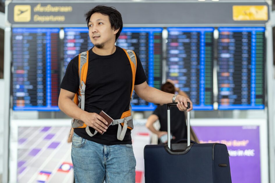 Portrait of Asian traveler with luggage with passport standing over the flight board at Passanger white plane lands. Blue airplane on the platform of Hartsfield-Jackson Atlanta International Airport (ATL) Runway. Landing aircraft
