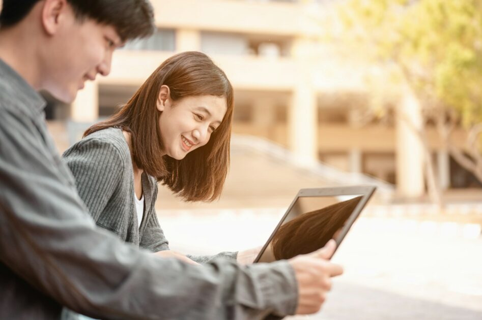 Two students reading the book and learning by laptop at stairs in university.