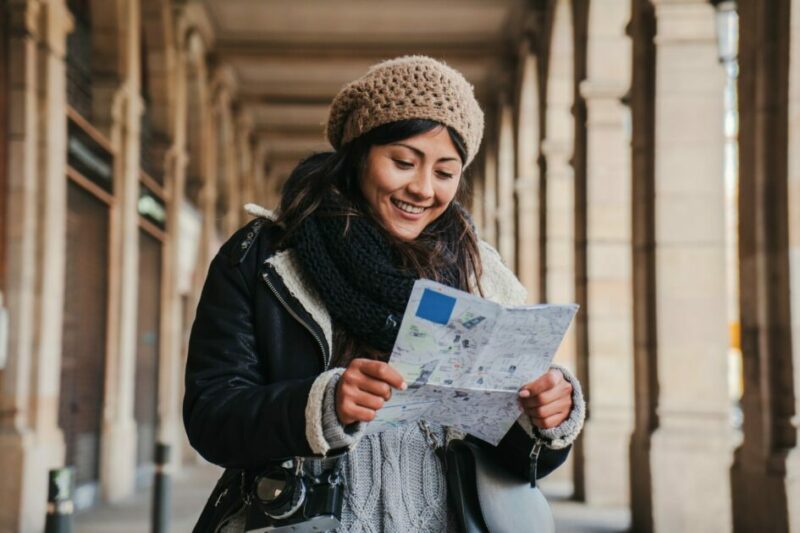 Young tourist woman smiling and reading a map to find the location of the european monument. Lost